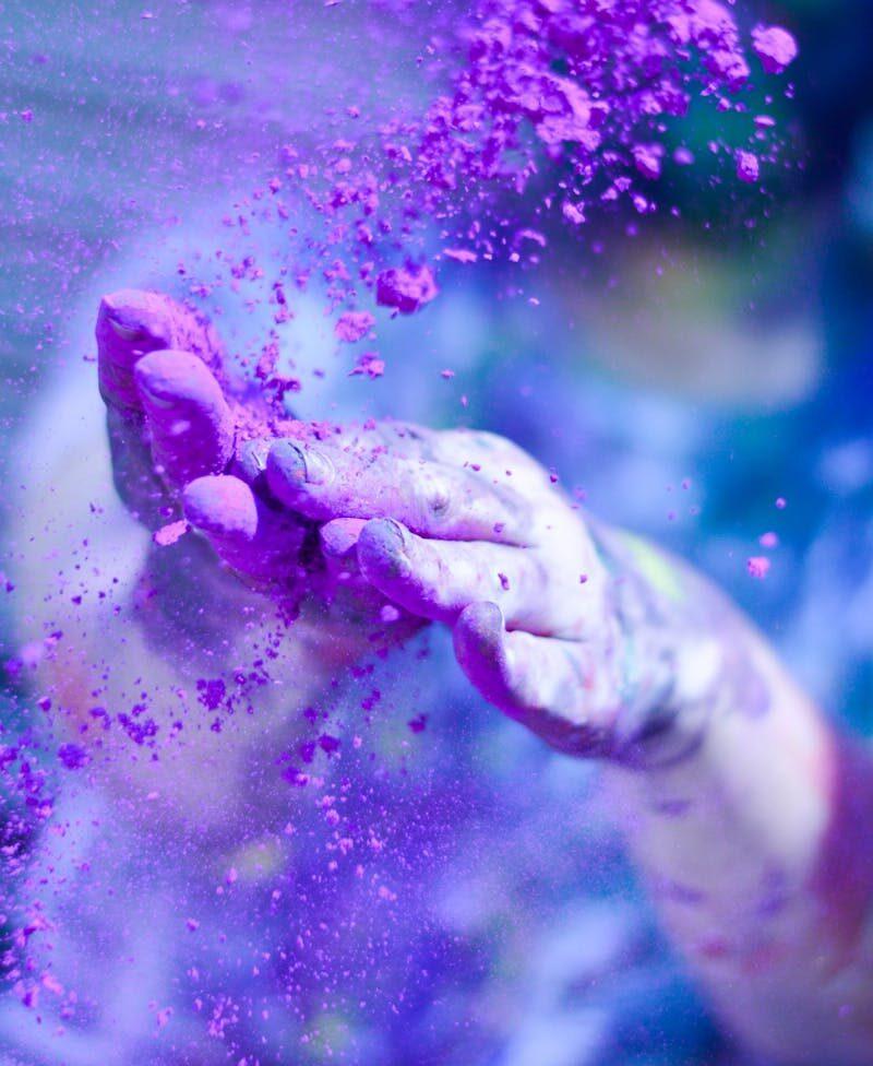 Close-up of hands throwing vibrant purple powder outdoors, capturing motion and color.